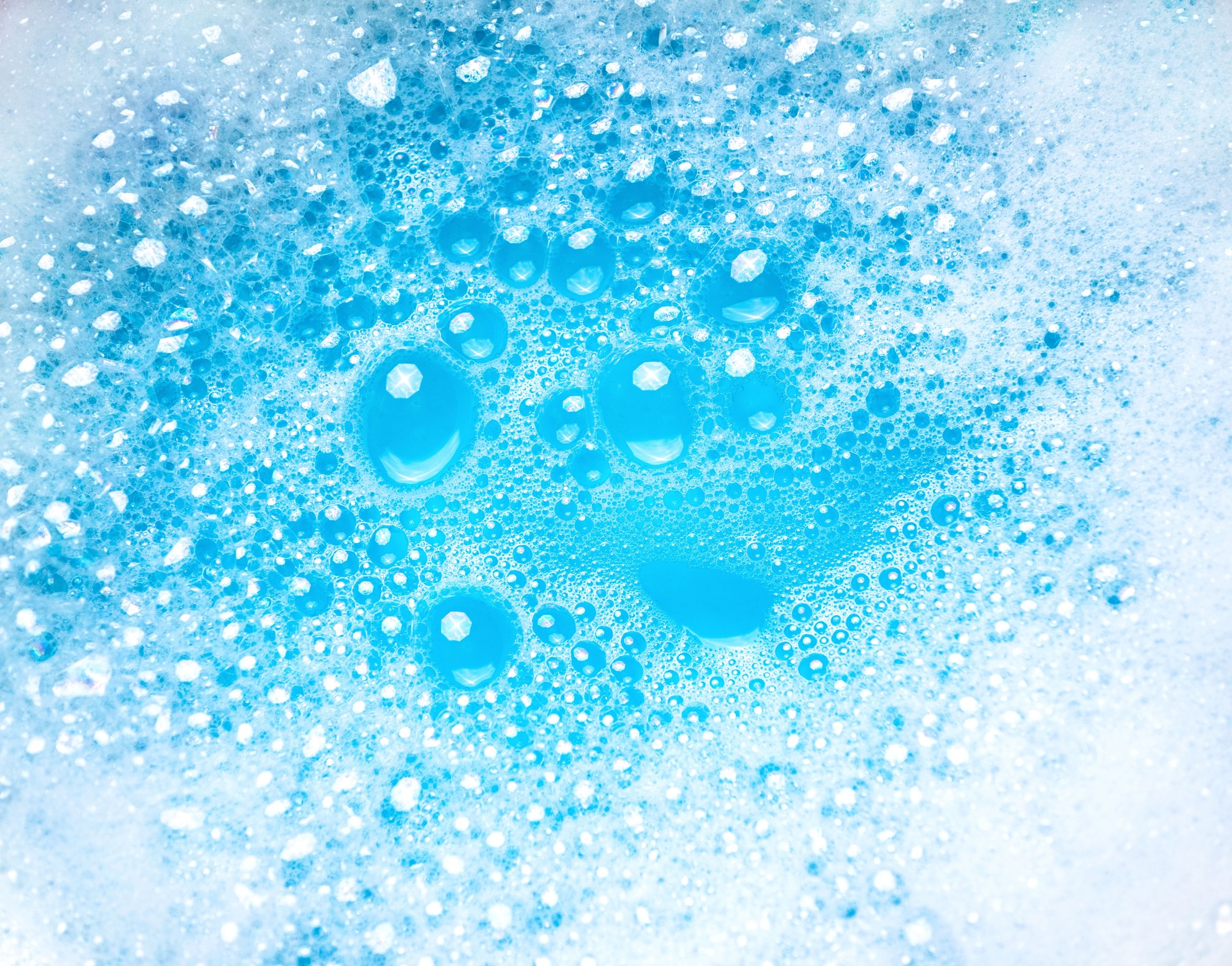 Small and big bubbles in blue water. Abstract white soap foam texture. Concept of cleaning and washing.